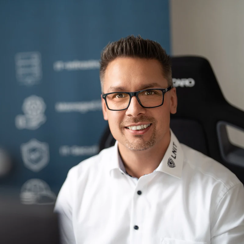 Lars Neumann, Gründer und Inhaber von LNIT aus Diekholzen, freundliches Lächeln im Büro vor dem LNIT-Banner