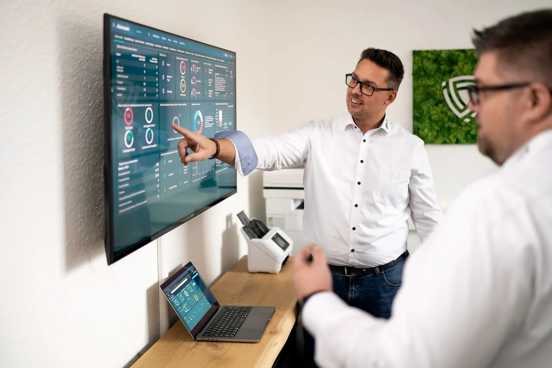 Lars Neumann erklärt einem Kollegen ein Dashboard auf einem Wandbildschirm