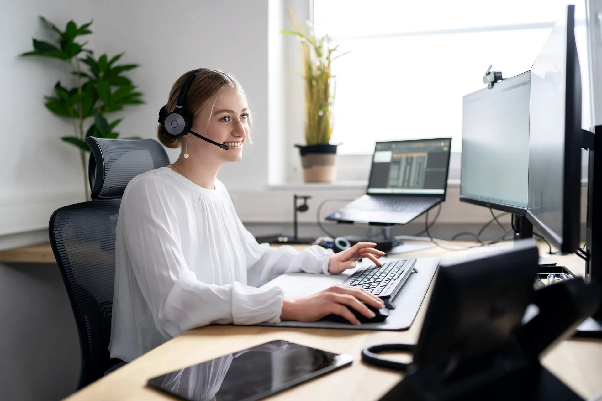 LNIT-Mitarbeiterin mit Headset arbeitet freundlich am Arbeitsplatz im hellen Büro